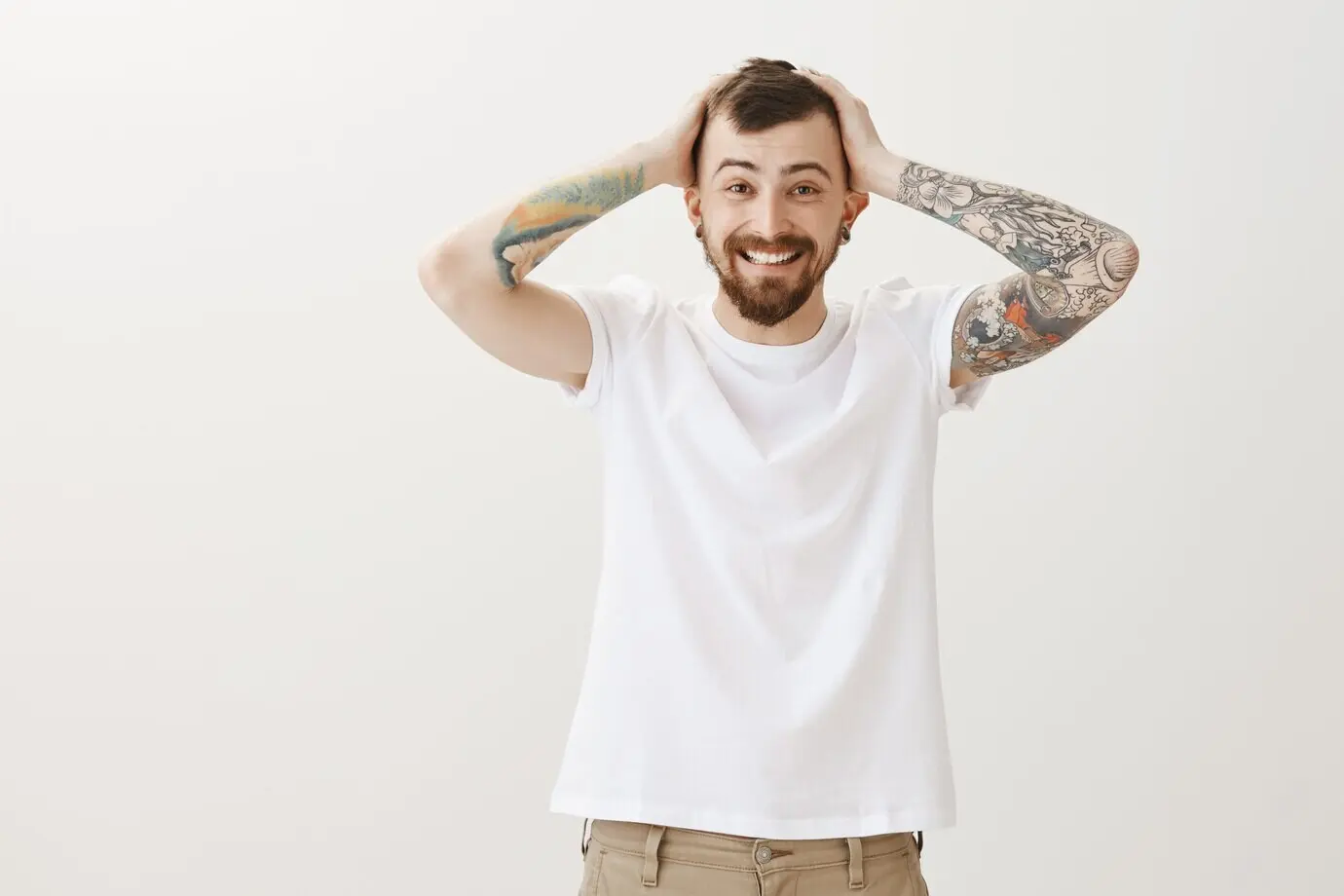 Glücklicher bärtiger Mann fasst sich an den Kopf, zufrieden mit dem neuen Haarschnitt.