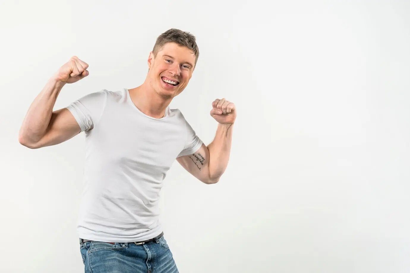 Porträt eines lächelnden jungen Mannes, der ihre Muskeln anspannt, vor weißem Hintergrund.